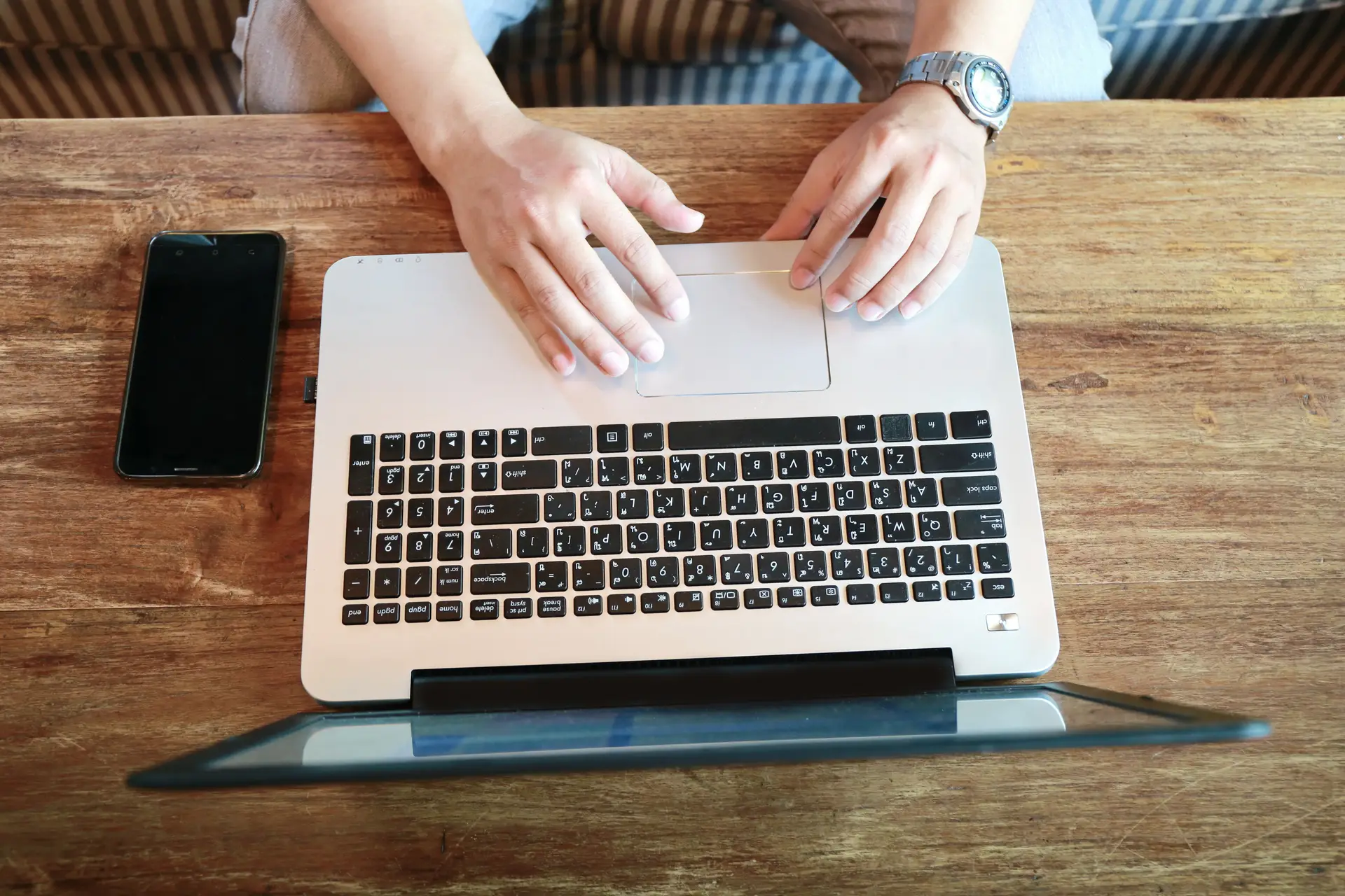 Man,Hand,Working,On,Phone,And,Laptop,On,Wooden,Table